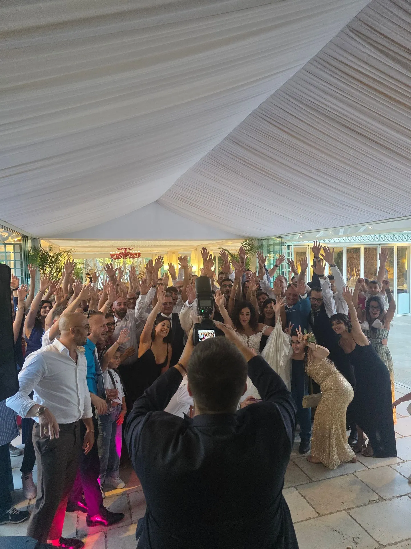 Foto di gruppo con la sposa e gli invitati, tutti con le mani alzate.